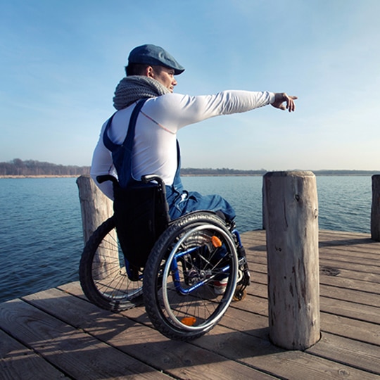 Man in wheelchair on a pier pointing into distance
